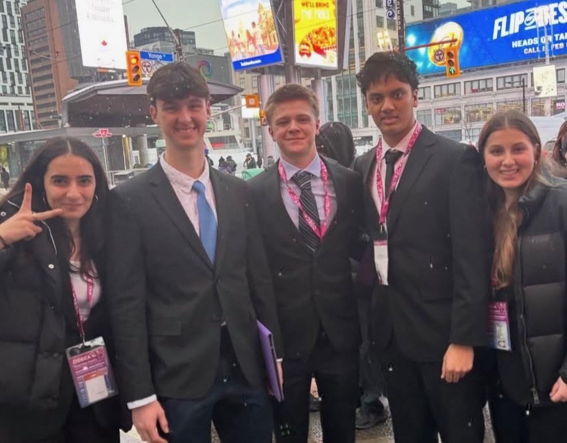 Five Mother Teresa DECA students in suits and competition lanyards, smiling at Yonge and Dundas in the snow